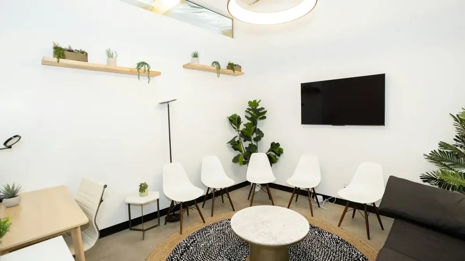 Lichte wachtkamer met witte stoelen, een ronde tafel en planten